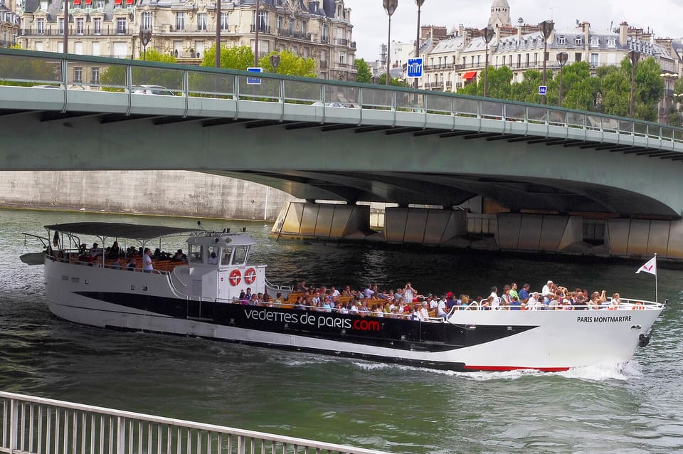 A Vedettes de Paris boat with an open deck passing under a bridge